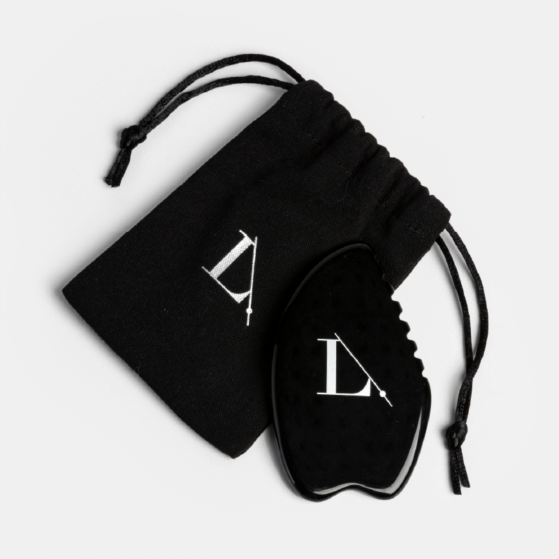 Le Gua Sha noir en obsidienne Limelife posé à côté de sa pochette de rangement noire en rPET avec cordon et logo assorti.