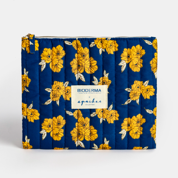 Vue de face de la trousse isotherme matelassée bleue à motif de fleurs jaunes, en suédine rPET, avec étiquette de collaboration Bioderma x Apaches.