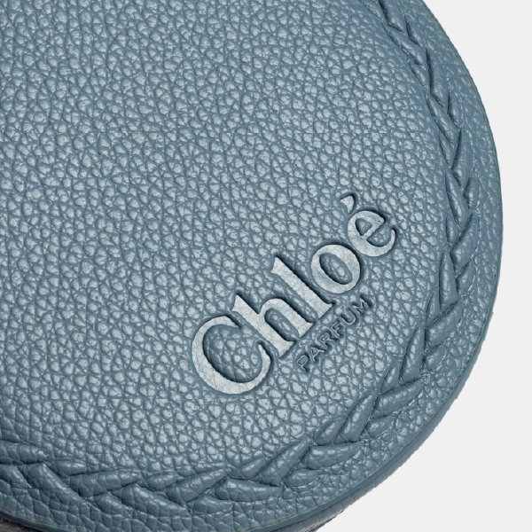 Gros plan sur le logo "Chloé Parfum" gravé en relief sur le couvercle en rPU grainé bleu, entouré d'un motif tressé décoratif.