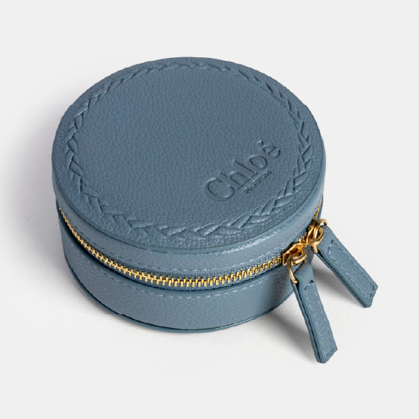 Boîte à bijoux ronde Chloé Nomade en rPU grainé bleu, avec son motif tressé en relief, sa fermeture éclair dorée et ses deux tirettes assorties.