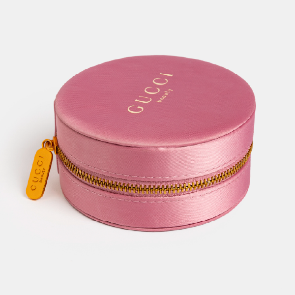 Boîte à bijoux ronde Gucci en satin de polyester recyclé rose poudré, fermée par un zip en métal doré.