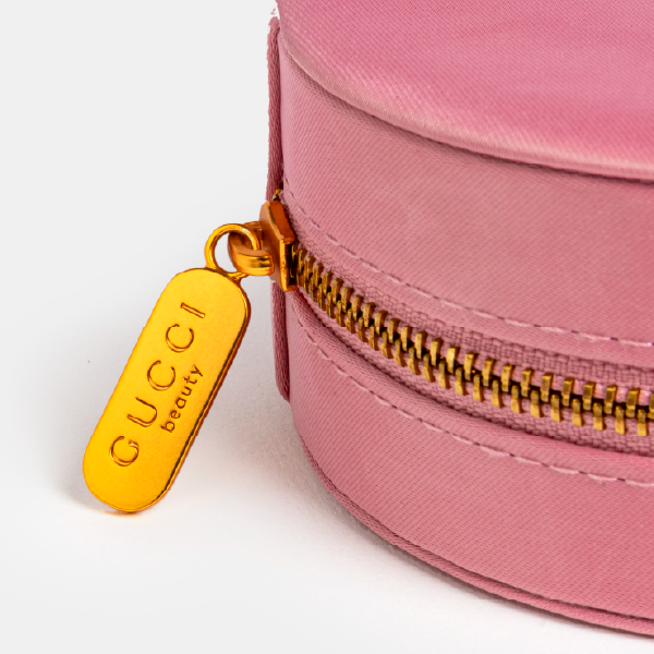 Gros plan sur la tirette en métal doré de la fermeture éclair, gravée du logo "GUCCI beauty", soulignant la finition de luxe de l'écrin.