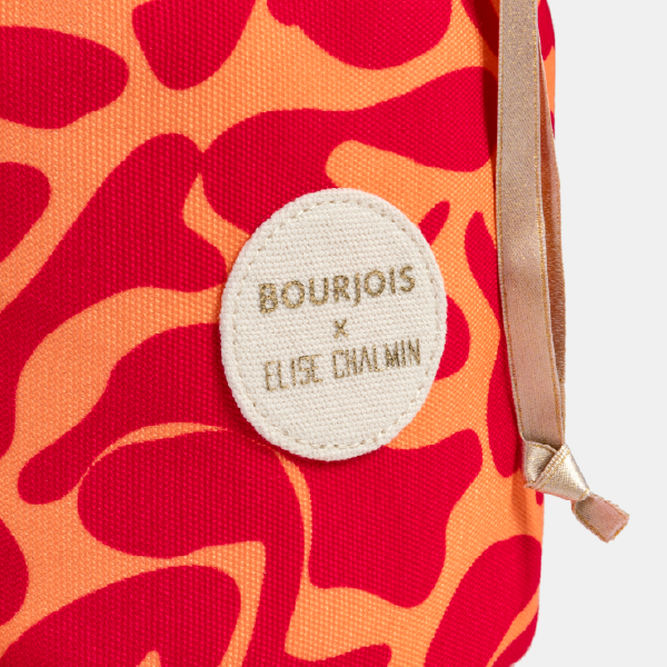 Gros plan sur l'étiquette en tissu cousue sur le pochon Bourjois x Elise Chalmin, au motif rouge et orange.