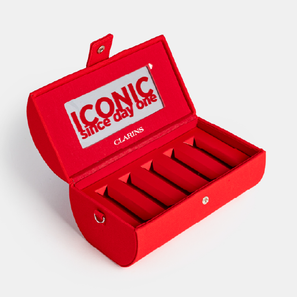 Coffret rouge Clarins ouvert et vide, montrant l'intérieur avec les compartiments et le miroir sur le rabat portant le slogan "ICONIC since day one".