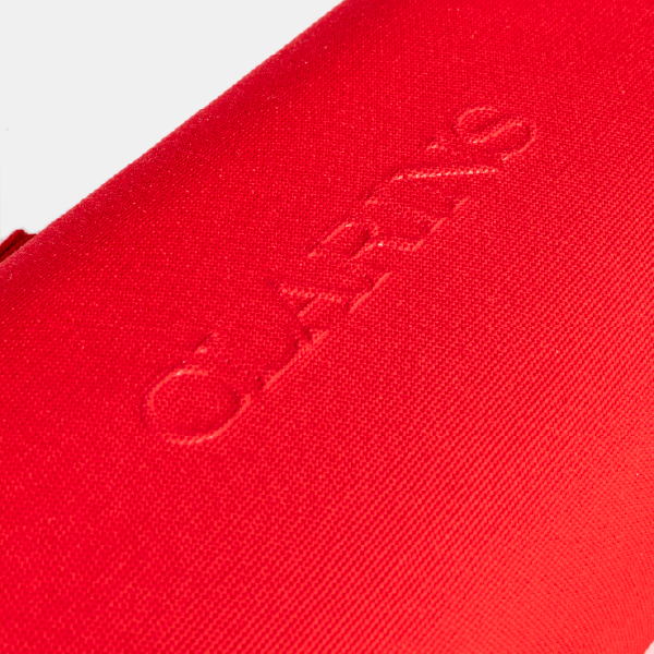 Gros plan sur la texture du tissu rPET rouge du coffret avec le logo Clarins embossé en relief.