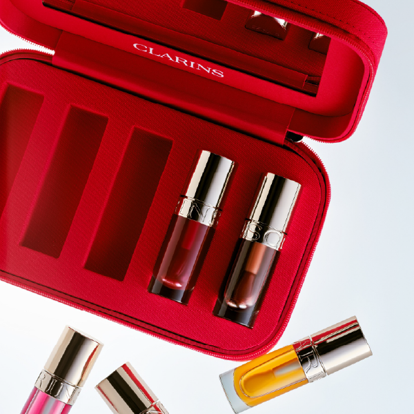 Trousse de voyage zippée rouge Clarins ouverte, avec des compartiments pour ranger des huiles à lèvres et un miroir intégré.