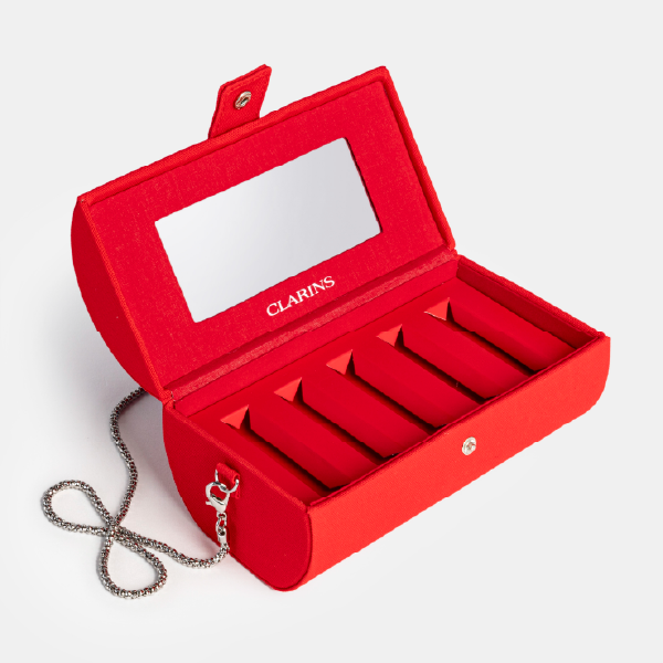 Le coffret rouge Clarins ouvert avec sa chaîne en métal argenté attachée, illustrant sa transformation en sac minaudière.