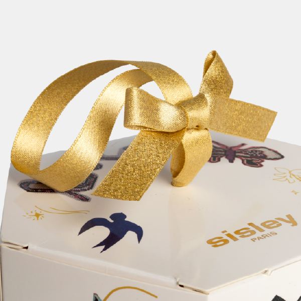 Gros plan sur le nœud du ruban doré scintillant, posé sur le couvercle du coffret hexagonal Sisley.