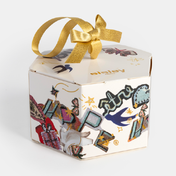 Vue de trois-quarts du coffret hexagonal Sisley, montrant les illustrations colorées sur les côtés, le logo doré et le ruban.