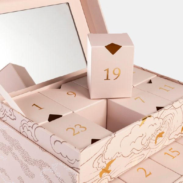 Gros plan sur l'intérieur du calendrier de l'Avent coiffeuse, montrant les boîtes numérotées en or et le miroir intégré dans le couvercle.