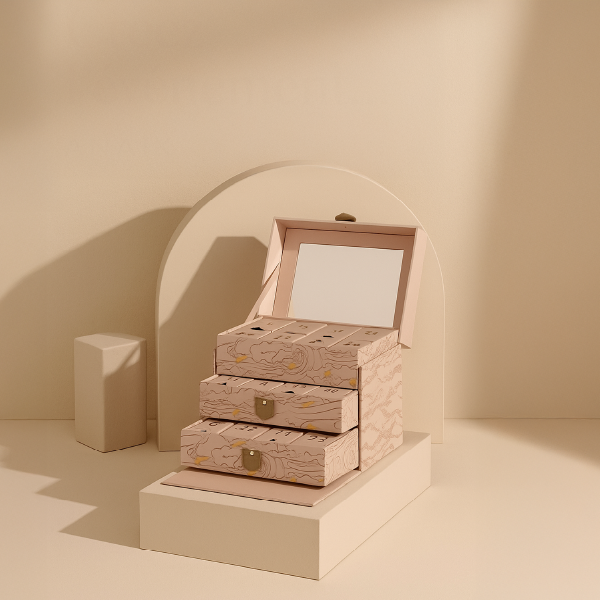 Le calendrier de l'Avent en forme de coiffeuse rose posé sur un podium, montrant sa structure à trois tiroirs dans un décor beige.