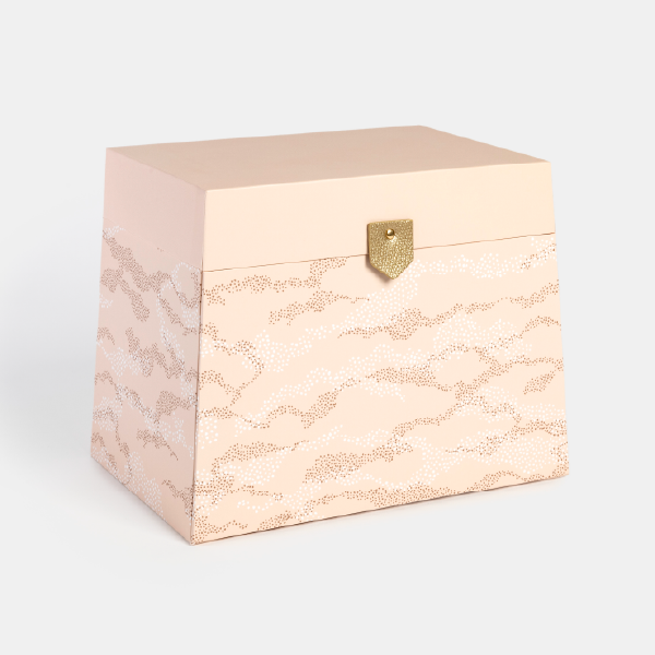 Vue de trois-quarts du calendrier de l'Avent coiffeuse fermé, montrant son design extérieur rose avec un motif de nuages et son fermoir doré.