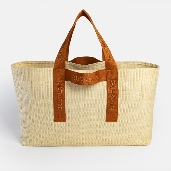 Vue de face du sac de plage Guerlain en Paperstraw certifié FSC, avec des anses en rPET terracotta siglées.