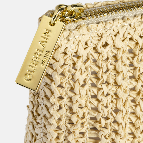 Zoom sur la tirette de zip en métal doré gravée "GUERLAIN PARIS", attachée à la trousse en Paperstraw.