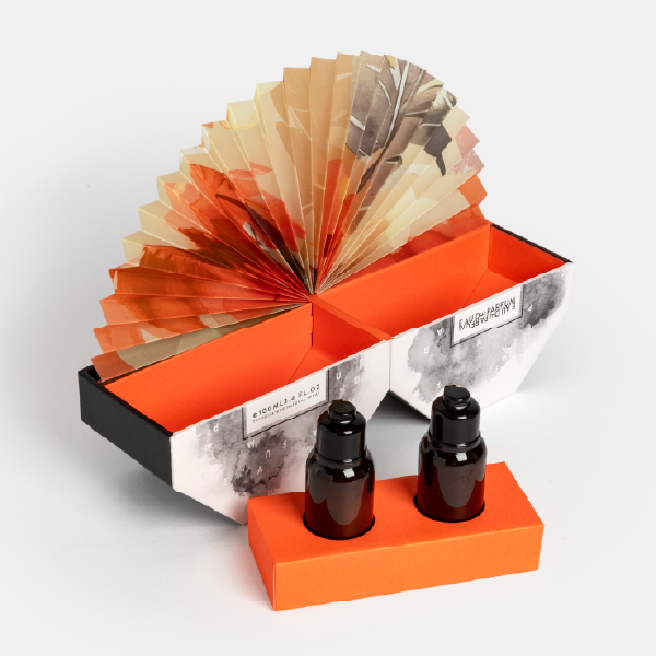 Le coffret éventail ouvert avec son insert orange et ses deux flacons posés à l'extérieur, montrant la structure et le pop-up déployé.