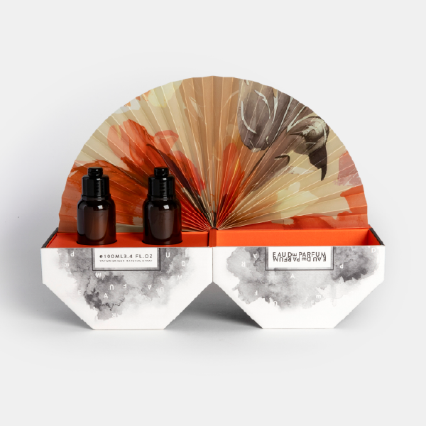 Vue du coffret parfum ouvert, révélant deux flacons de parfum dans leurs emplacements et l'éventail en papier déployé en arrière-plan.