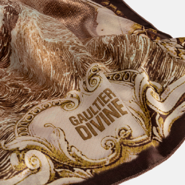 Gros plan sur le coin du furoshiki en soie montrant le logo "GAULTIER DIVINE" imprimé dans un cartouche de style baroque.