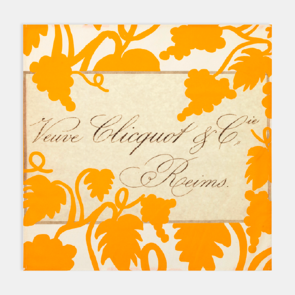 Gros plan sur le design du furoshiki déplié, montrant le motif de vigne orange et l'étiquette centrale avec la calligraphie "Veuve Clicquot".
