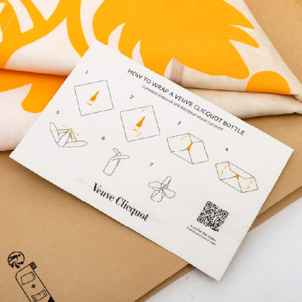 Gros plan sur la carte d'instructions, montrant les schémas de pliage pour emballer une bouteille, avec un QR code pour la vidéo.