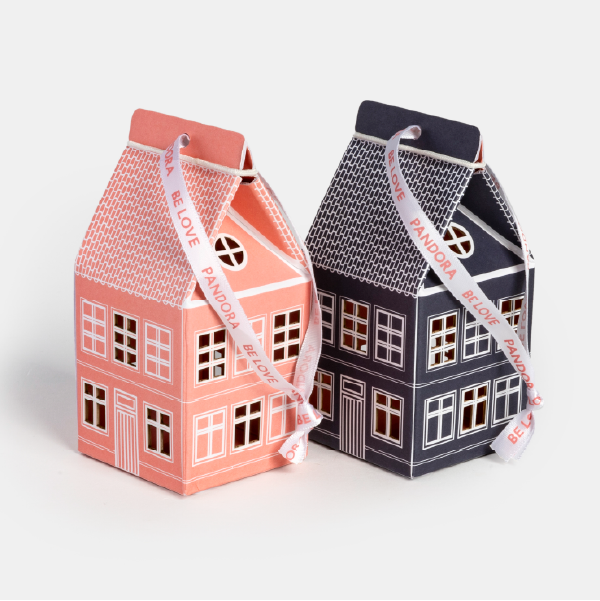 Les deux variations de couleur des maisonnettes en papier Pandora, rose et bleu foncé, posées côte à côte et fermées par un ruban siglé.