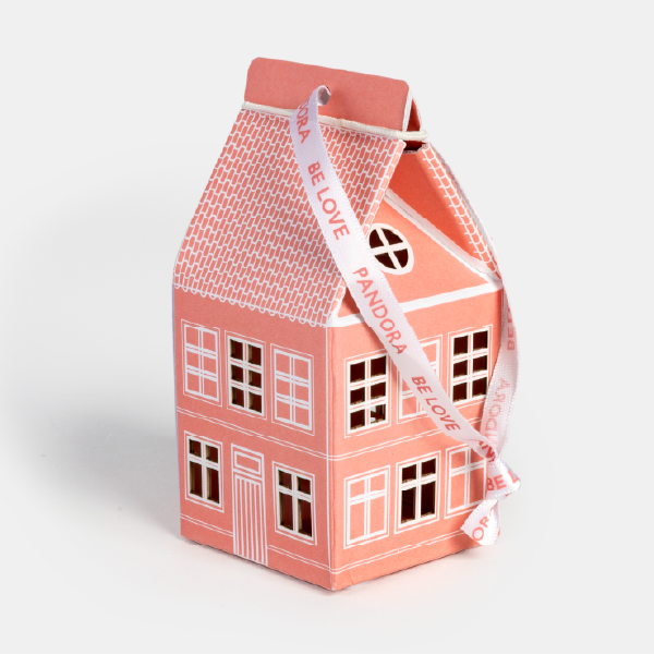 La maisonnette en papier rose Pandora, vue de trois-quarts, fermée par son ruban blanc siglé "PANDORA BE LOVE".