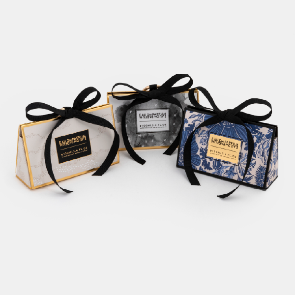 Vue de groupe des trois mini bags de la collection Anaïk, chacun avec un motif différent (pois, floral bleu, aquarelle), tous fermés par un ruban noir et un anneau mousqueton doré.