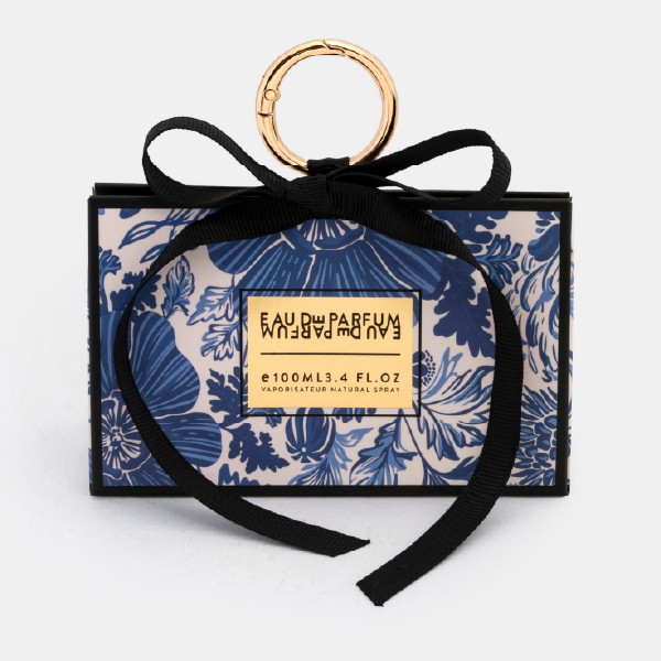Le mini bag fermé en forme de trapèze avec un motif floral bleu et blanc, un ruban noir noué et un anneau mousqueton doré.