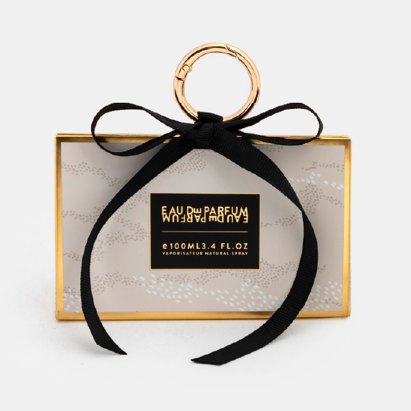 Le mini bag fermé avec un motif de pois sur fond crème, des bordures dorées, un ruban noir noué et un anneau mousqueton doré.