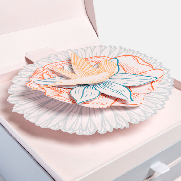 Gros plan sur le mécanisme de pop-up en papier du calendrier, représentant une fleur et un oiseau en couches de papier coloré.