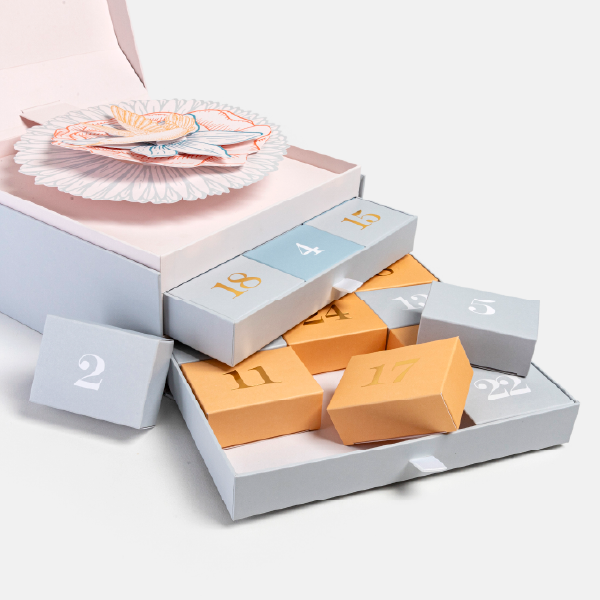 Les deux tiroirs du calendrier de l'Avent sont sortis, avec plusieurs des petites boîtes numérotées (orange et bleu-gris) posées en vrac.