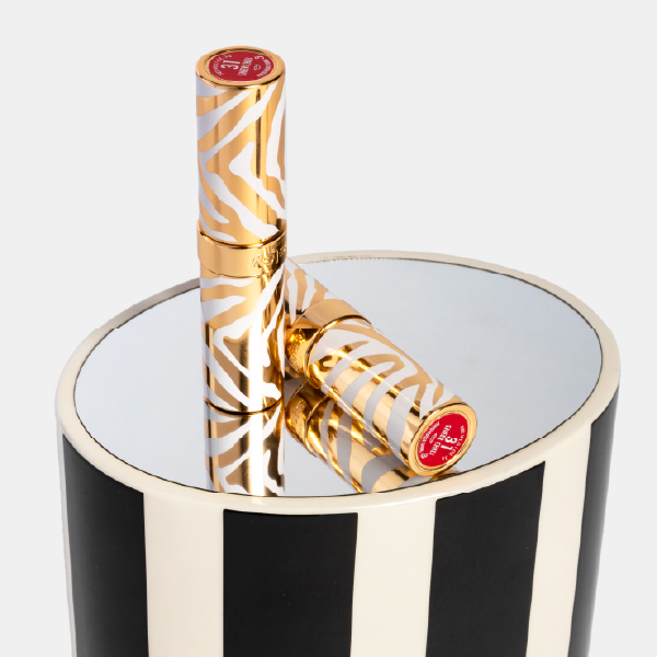Deux rouges à lèvres au packaging zèbre or et blanc posés sur le couvercle miroir du coffret en bois laqué à rayures.
