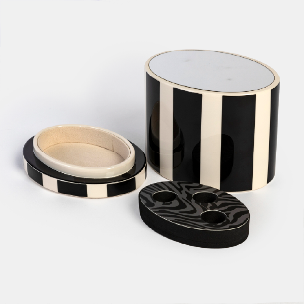 Vue éclatée du coffret Anaïk montrant ses différents composants : le pot cylindrique à rayures, le couvercle-socle doublé pour bijoux, et l'insert amovible à motif zébré pour ranger quatre rouges à lèvres.