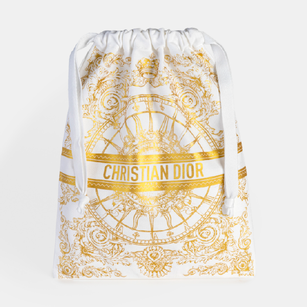 Pochon Christian Dior de la collection de Noël en coton recyclé brossé blanc, avec les cordons de serrage tirés, mettant en valeur l'impression dorée d'inspiration baroque.