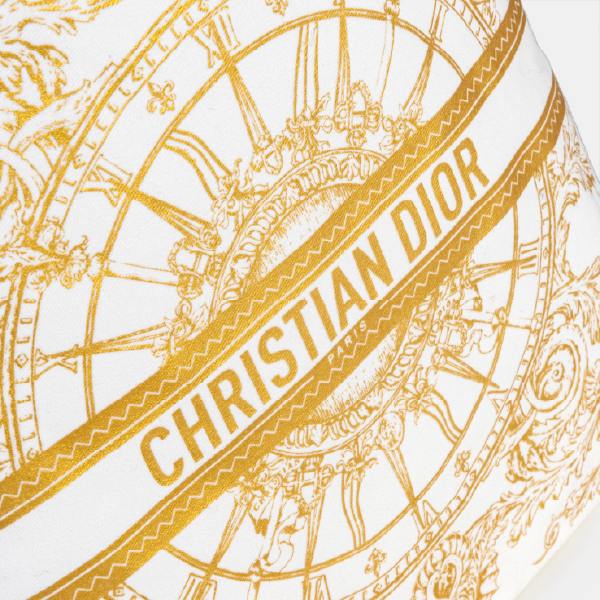 Gros plan sur l'impression dorée fine et précise du pochon Dior, montrant les détails du motif d'horloge et la bande centrale avec l'inscription "CHRISTIAN DIOR PARIS".