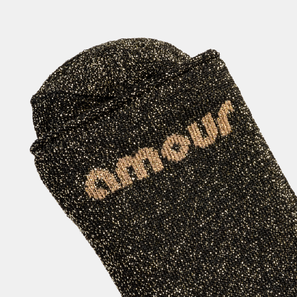 Gros plan sur la paire de chaussettes noires à paillettes dorées, avec le mot "Amour" tissé en doré.