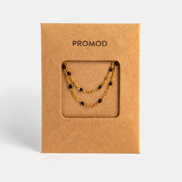 Le collier double rang à chaîne dorée et perles noires, présenté sur son support en carton kraft siglé Promod.