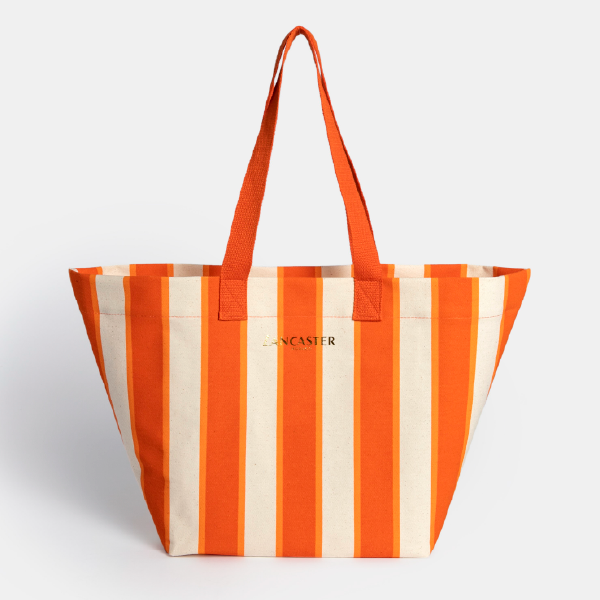 Vue de face du sac de plage Lancaster en coton bio, affichant son motif à rayures verticales orange et blanches et son logo central.