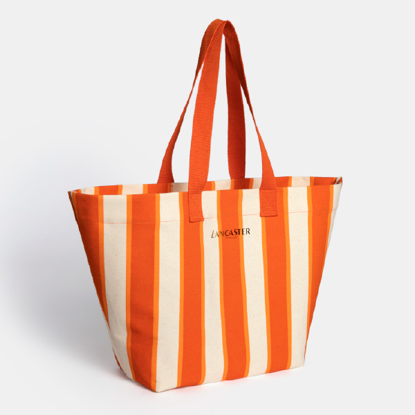 Vue de trois-quarts du sac de plage Lancaster à rayures, montrant sa forme tote généreuse et ses anses en coton orange.