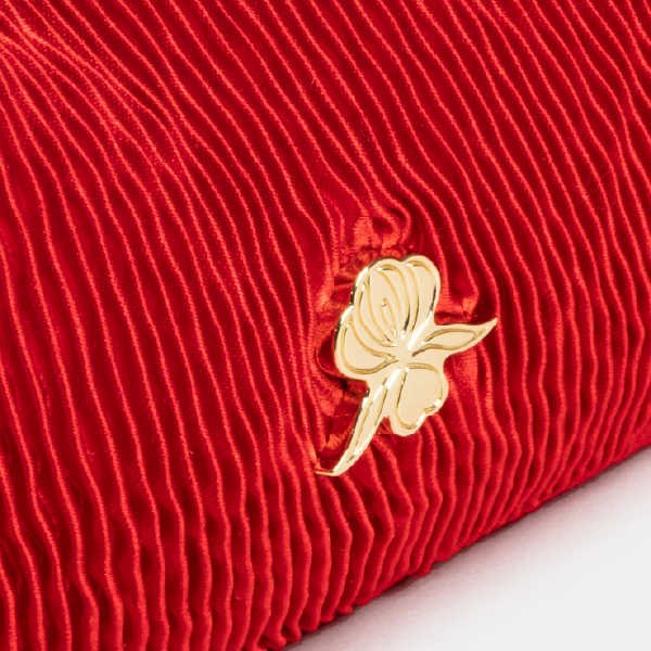 Gros plan sur le monogramme Sisley en métal doré en forme d'orchidée de Sisley, posé sur la texture soyeuse du satin plissé rouge.