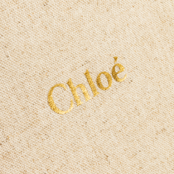 Gros plan sur le logo Chloé en marquage doré à chaud, appliqué sur la texture naturelle du tissu en lin et viscose.