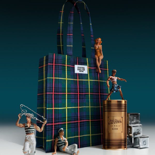 Mise en scène du tote bag tartan Jean Paul Gaultier avec le parfum Le Mâle Elixir et des figurines emblématiques de la marque.