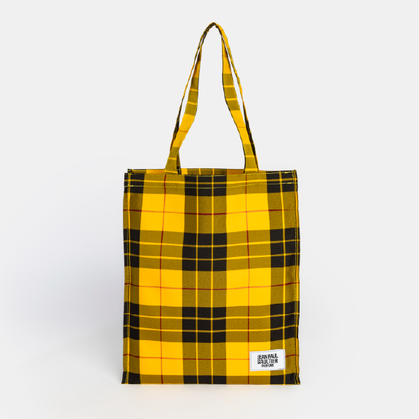 Vue de face du tote bag Jean Paul Gaultier en tartan jaune et noir, avec son étiquette logo blanche.