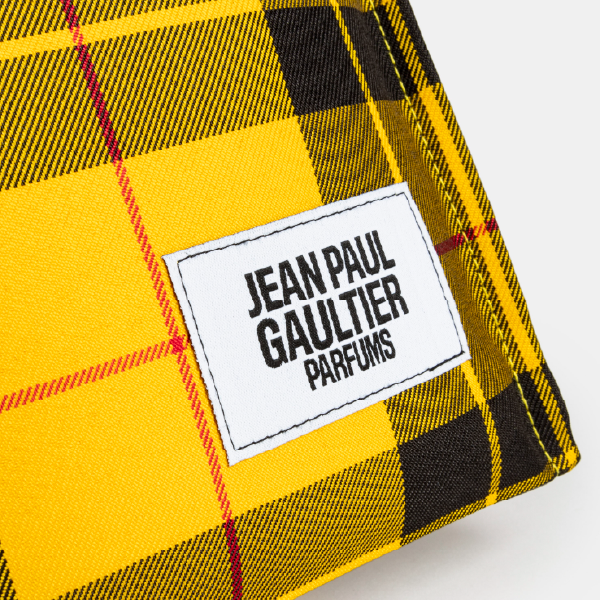 Gros plan sur l'étiquette blanche "JEAN PAUL GAULTIER PARFUMS", cousue sur le tissu à motif tartan jaune et noir du tote bag.