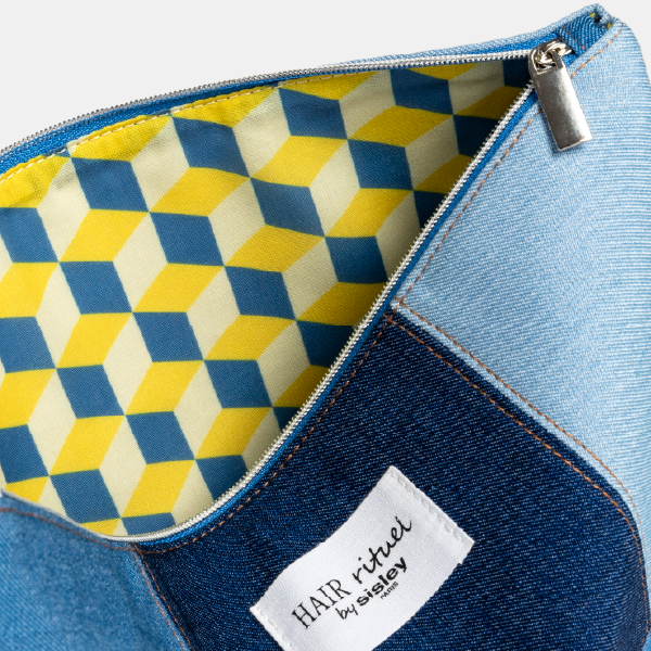 Vue de l'intérieur de la trousse Sisley, révélant une doublure en RPET avec un motif géométrique 3D audacieux en jaune, bleu et blanc, contrastant avec l'extérieur en denim.
