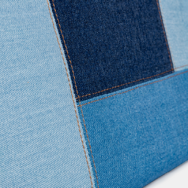 Gros plan sur les surpiqûres couleur tabac de la trousse, soulignant la jonction précise entre les différents empiècements de denim effet patchwork.