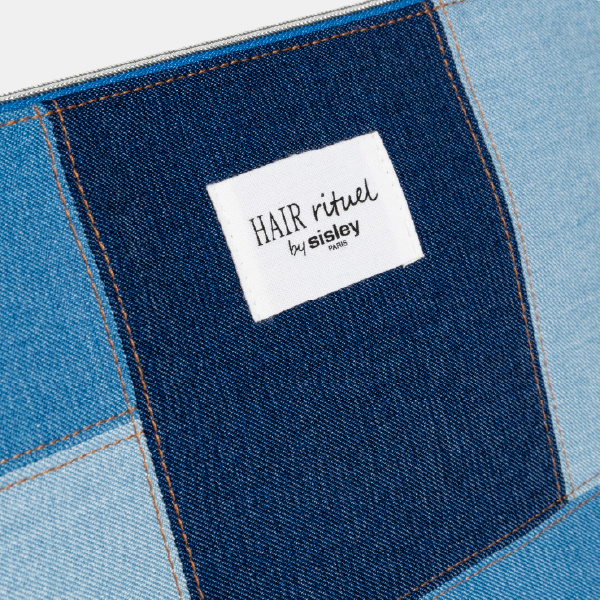 Zoom sur l'étiquette logo blanche "HAIR rituel by sisley" en Jacquard RPET, cousue sur un empiècement en denim bleu foncé.