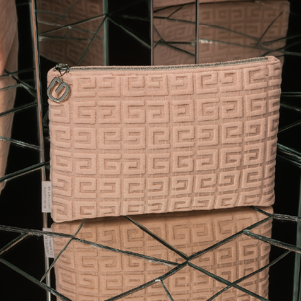 Trousse Givenchy avec motif monogramme en relief, présentée dans un décor de miroirs qui reflètent son design sophistiqué.