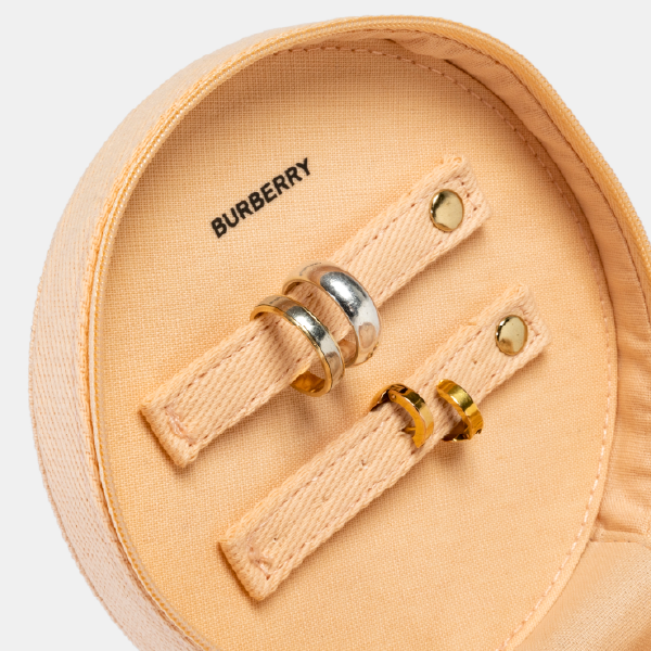Gros plan sur les rangements pour bagues dans le couvercle de la trousse Burberry, avec des lanières en coton et des boutons-pression en métal doré.