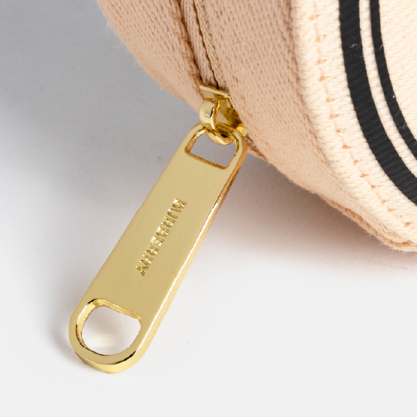 Gros plan sur la tirette en métal doré brillant, gravée du logo Burberry, illustrant la finition haut de gamme de la trousse.