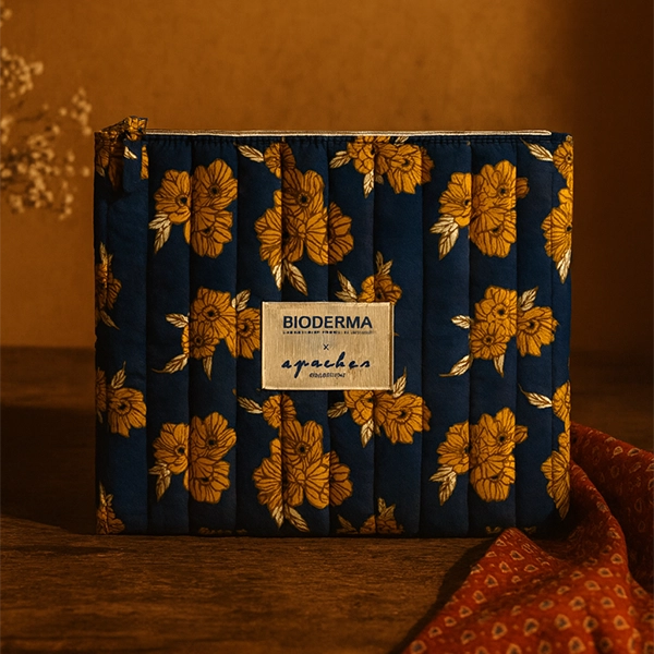 Trousse matelassée Bioderma x Apaches Collections en tissu bleu imprimé fleuri jaune, présentée dans une mise en scène chaleureuse et élégante.